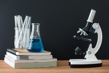 science laboratory test tubes and white microscope on wooden table with black background , laboratory equipment