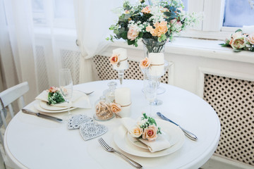 Interior design of white evening room with beautiful chandelier under served table with flowers on it. Big windows at the background. Vertical