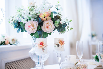 Interior design of white evening room with beautiful chandelier under served table with flowers on it. Big windows at the background. Vertical