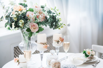 Interior design of white evening room with beautiful chandelier under served table with flowers on it. Big windows at the background. Vertical