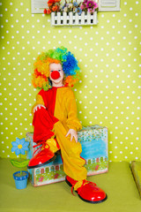 Obraz na płótnie Canvas A cheerful clown in an iridescent wig and huge boots stands on a luscious bright green background in polka dots