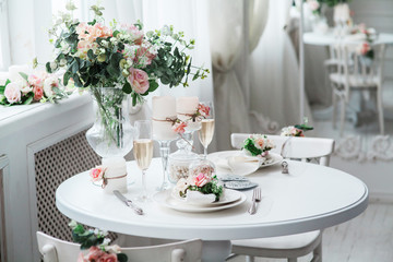 Interior design of white evening room with beautiful chandelier under served table with flowers on it. Big windows at the background. Vertical