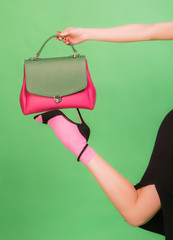 Fashion styled woman holding green and pink handbag on her foot on green background, concept photo