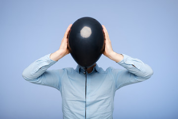 A white man covers his face with a black balloon. Hiding from problems