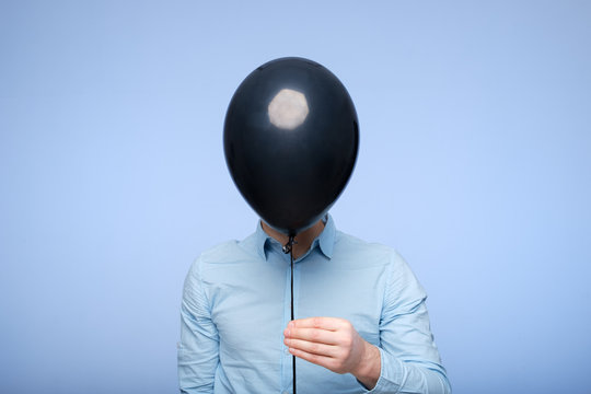 A white man covers his face with a black balloon. Hiding from problems