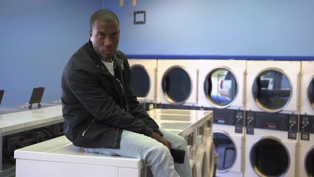 Young Male Dancing To Music At Laundromat Points At Camera.
