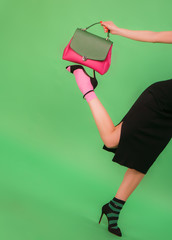 Fashion styled woman holding woman's handbag on a foot on green background