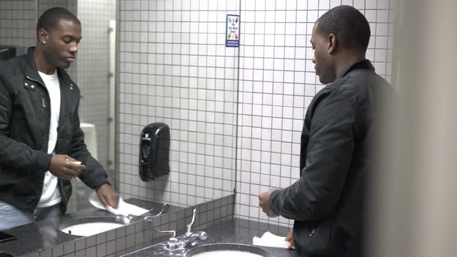 Young African American male standing in front of mirror in bathroom looking at himself as he gets ready.
