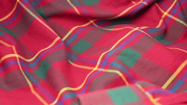 Tilt down shot of red plaid fabric reveals a cuff with a white button.