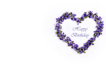 Fototapeta na wymiar Delicate spring violets in the shape of a heart on a white background. Happy birthday