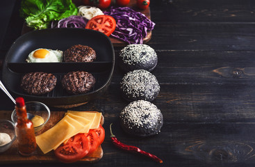 Ingredients for a black burger on a wooden surface
