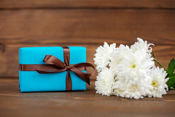 Wooden background with a gift and flowers for congratulations. The concept of Mother's Day, birthday, March 8.