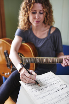 a young woman with a guitar, writing music.