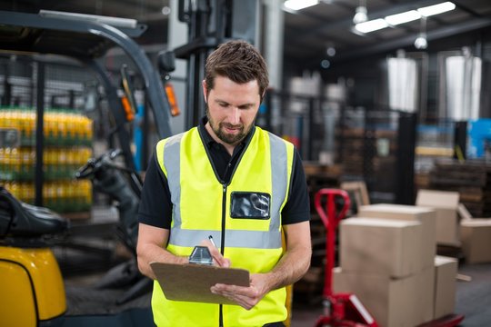 Factory worker writing on clipboard in factory