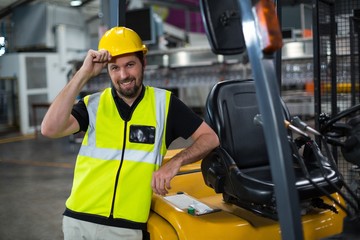 Portrait of smiling factory worker leaning on forklift