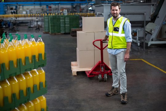 Factory worker pulling trolley of cardboard boxes in factory
