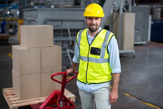 Factory worker pulling trolley of cardboard boxes in factory