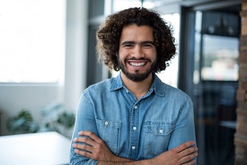 Smiling business executive standing with arms crossed in office