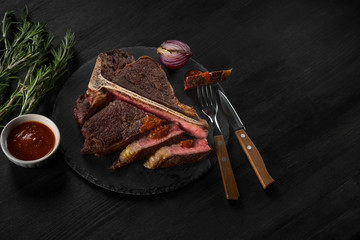 Steak meat with vegetables on a plate and pan grill. Black table background with brown textile. Copy text area for menu design. Horizontal top view