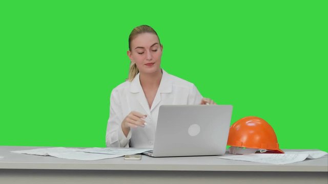 Tired young woman in safety helmet yawning and try to work on a Green Screen, Chroma Key.