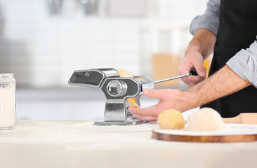 Man rolling dough for pasta on table, closeup
