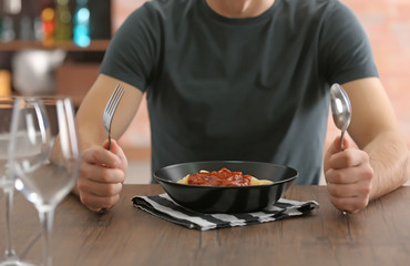 Young man eating pasta at table