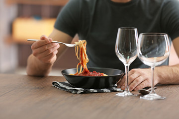 Young man eating pasta at table, closeup