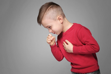 Cute little boy coughing on gray background