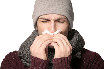 Young man using tissue to blow his nose on light background