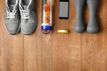 Fitness tracker and sports clothing with dumbbells on wooden floor, top view