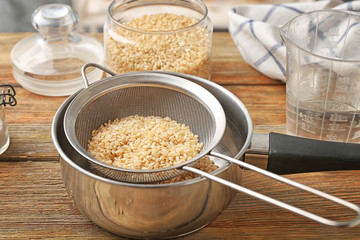 Sieve with raw brown rice in pan on wooden table