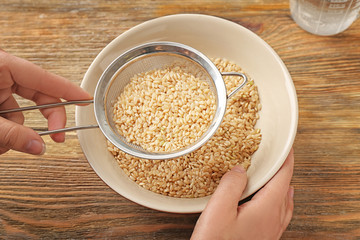 Female hand filling bowl with brown rice on wooden background