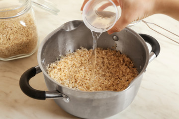 Female hand pouring water into pan with brown rice, closeup