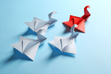Boss vs Leader concept. White origami birds behind red one on blue background