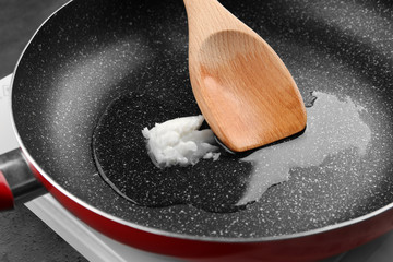 Wooden spoon with coconut oil on frying pan