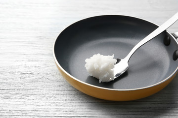 Spoon with coconut oil in frying pan on wooden table
