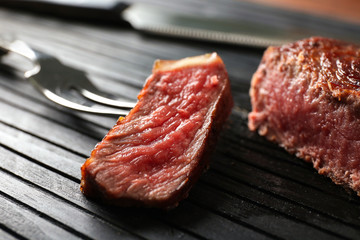 Delicious medium rare steak and fork with sliced piece on black wooden board