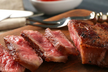 Sliced pieces of delicious medium rare steak on wooden board