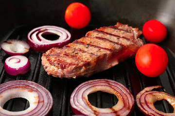 Preparing of steak with onion rings and tomatoes on grill pan, closeup