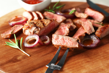 Fork with sliced piece of delicious grilled steak on wooden board