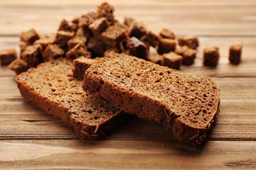 Sliced rye bread with seeds and croutons on wooden background