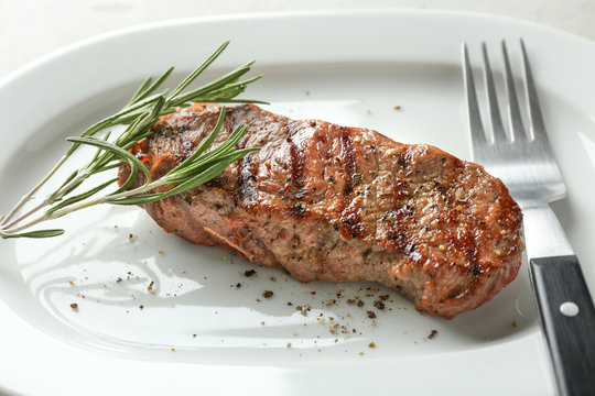 Delicious grilled steak with aromatic rosemary on white plate, closeup