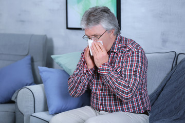 Senior man blowing nose on tissue at home