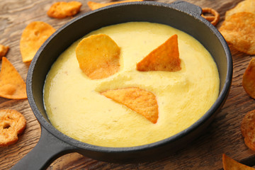 Frying pan with creamy cheese, chips and crackers on wooden background