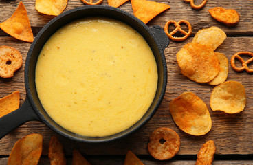 Frying pan with creamy cheese, chips and crackers on wooden background