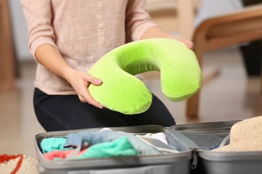 Woman with travel pillow packing suitcase at home