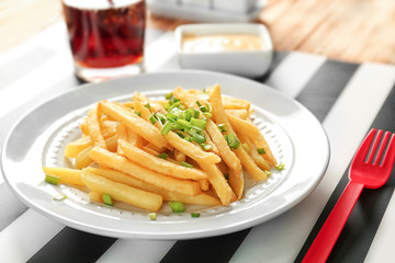 Portion of delicious french fries with onion on dining table