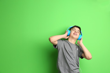 Teenager with headphones listening to music on color background