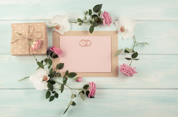 Pink roses, orchid, bridal rings and gift box with emty paper for wedding invitations