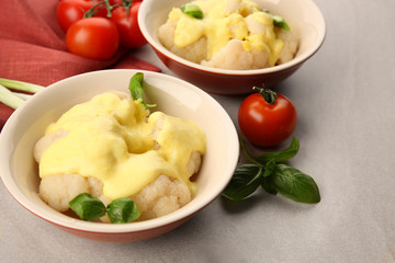 Bowls of delicious cauliflower with cheese sauce and vegetables, closeup